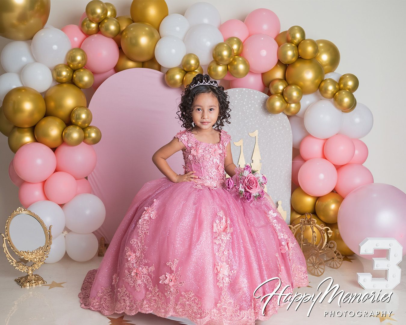 Princess themed first birthday setup with pink and gold balloon arch and sparkly decorations.