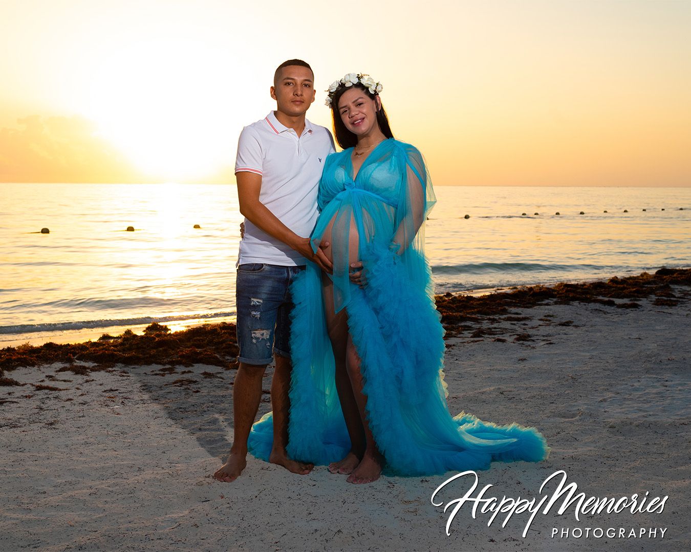 Couple poses on beach at sunset for maternity photo in flowing turquoise dress.
