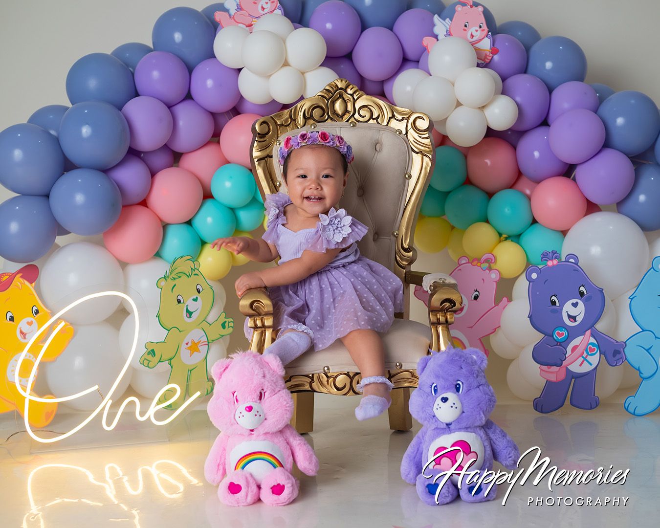 Pastel balloon arch with purple, blue, and pink balloons adorned with teddy bear decorations and floral accents.