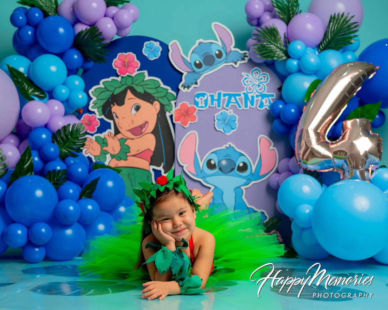 Festive balloon arch display in shades of blue and purple with tropical greenery for a party backdrop.