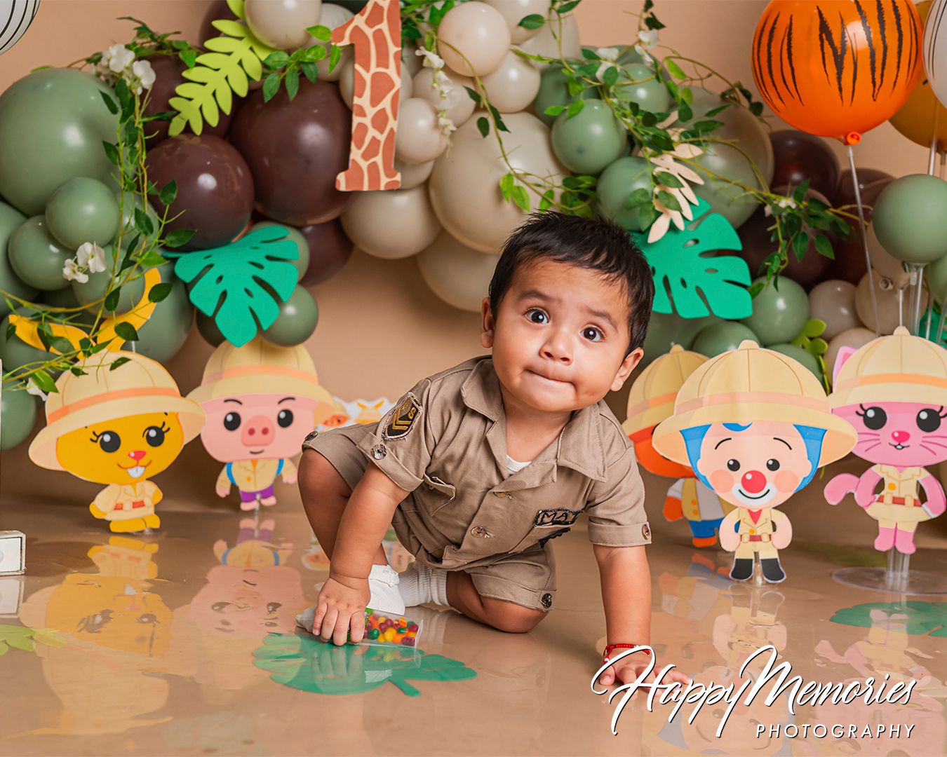 Safari-themed photo backdrop with giraffe prints, green balloons, and cute animal cartoon decorations.