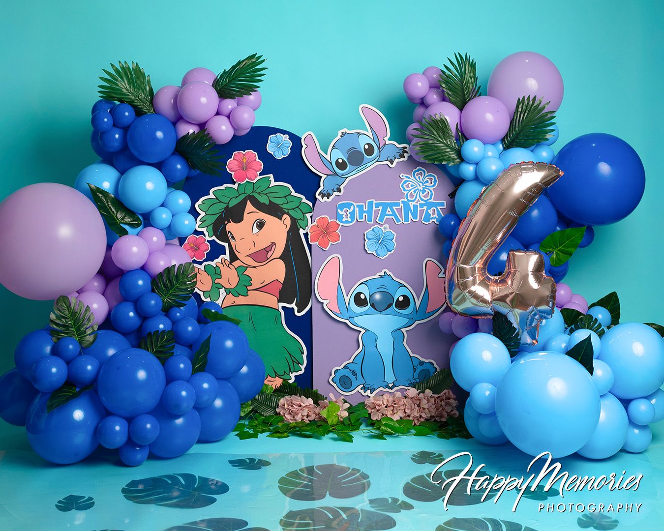 Blue and purple balloon arch with tropical palm leaves and cartoon character cutouts for a birthday party decoration.