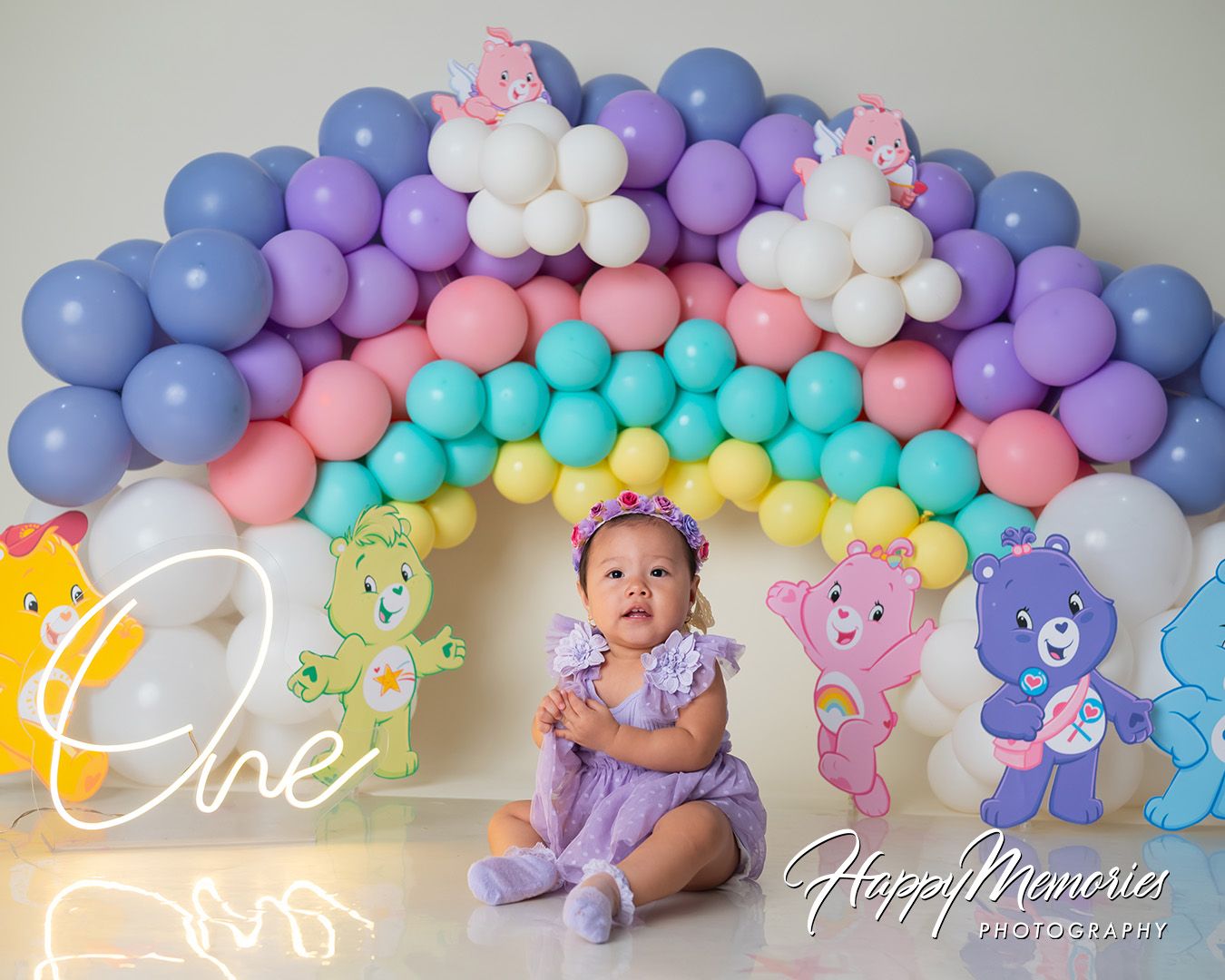 Pastel balloon arch display featuring purple, pink, blue, and turquoise balloons with white cloud-like accents.