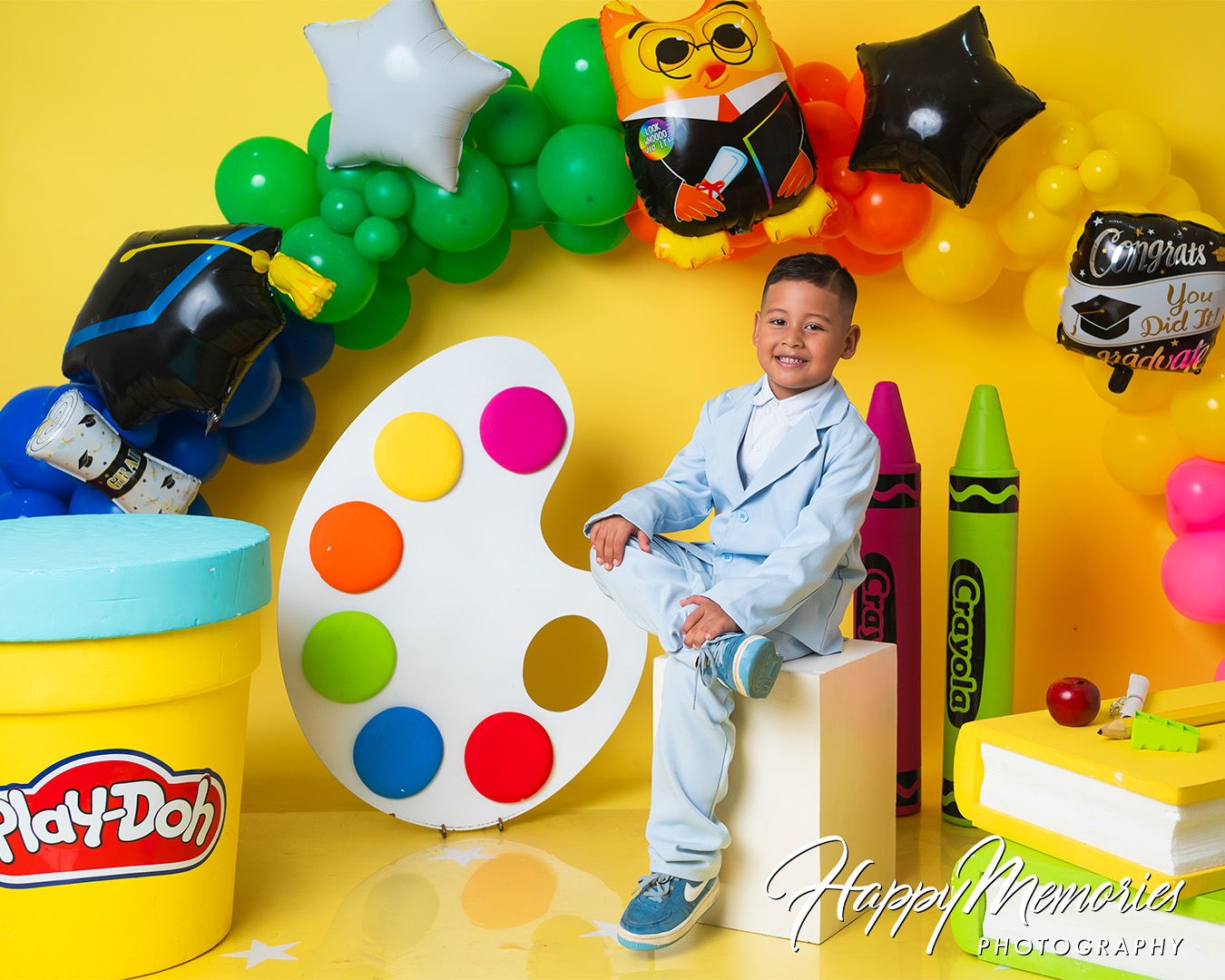 Artistic graduation photo setup with Play-Doh, paint palette props and balloon decorations.