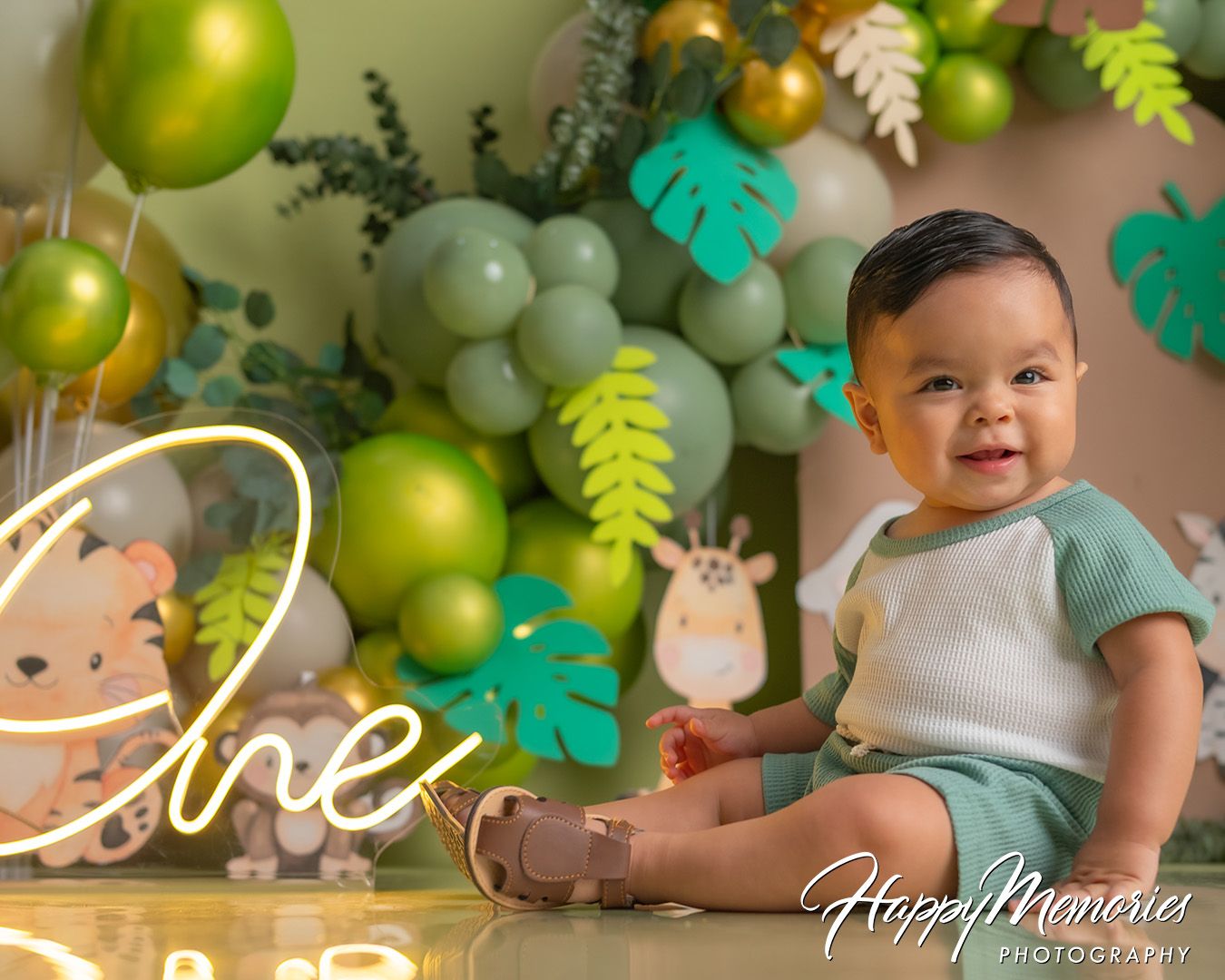 Green and gold balloon arch with tropical leaf decorations creates a festive party backdrop.