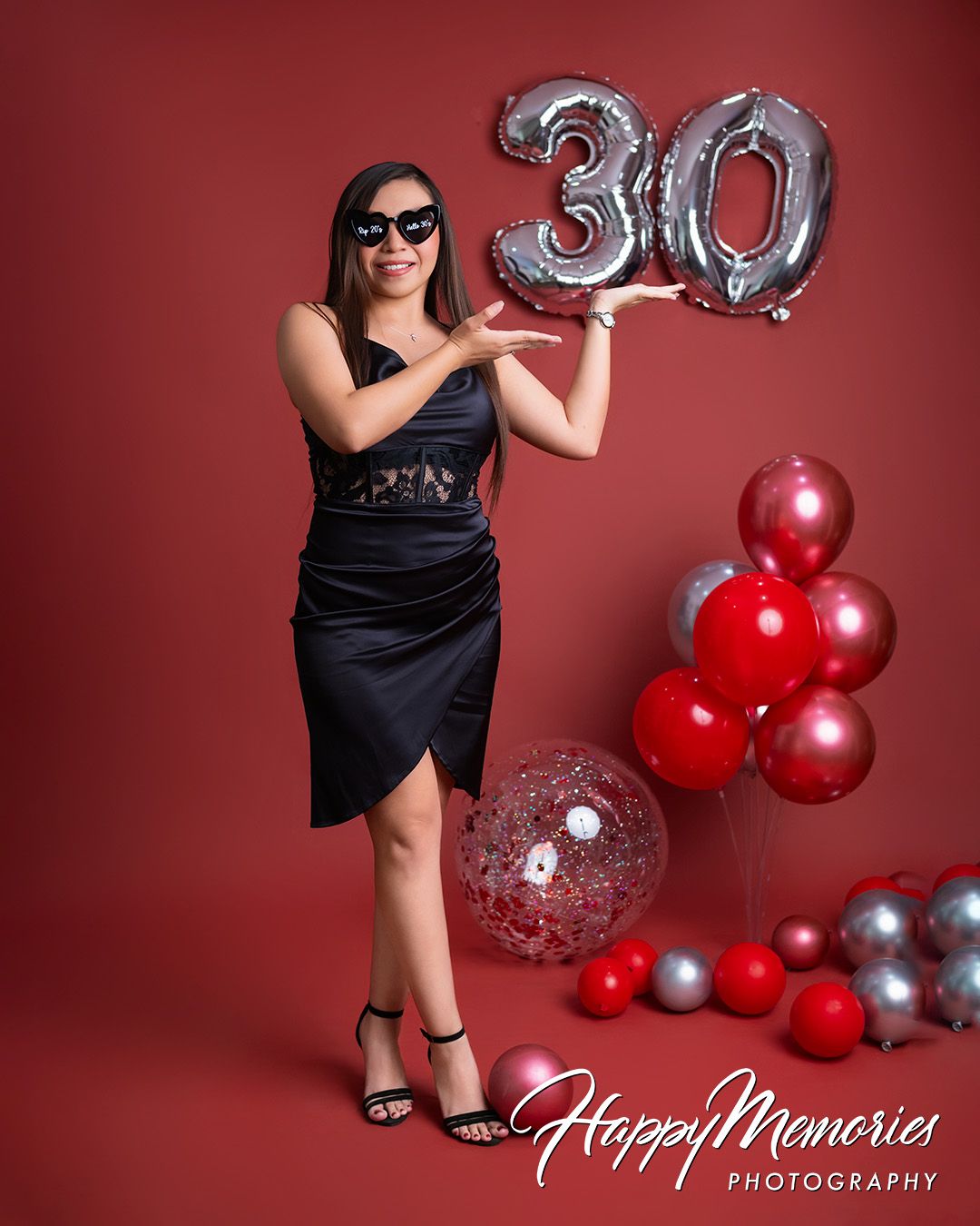 Stylish photo shoot with black dress and red balloons against a burgundy backdrop.