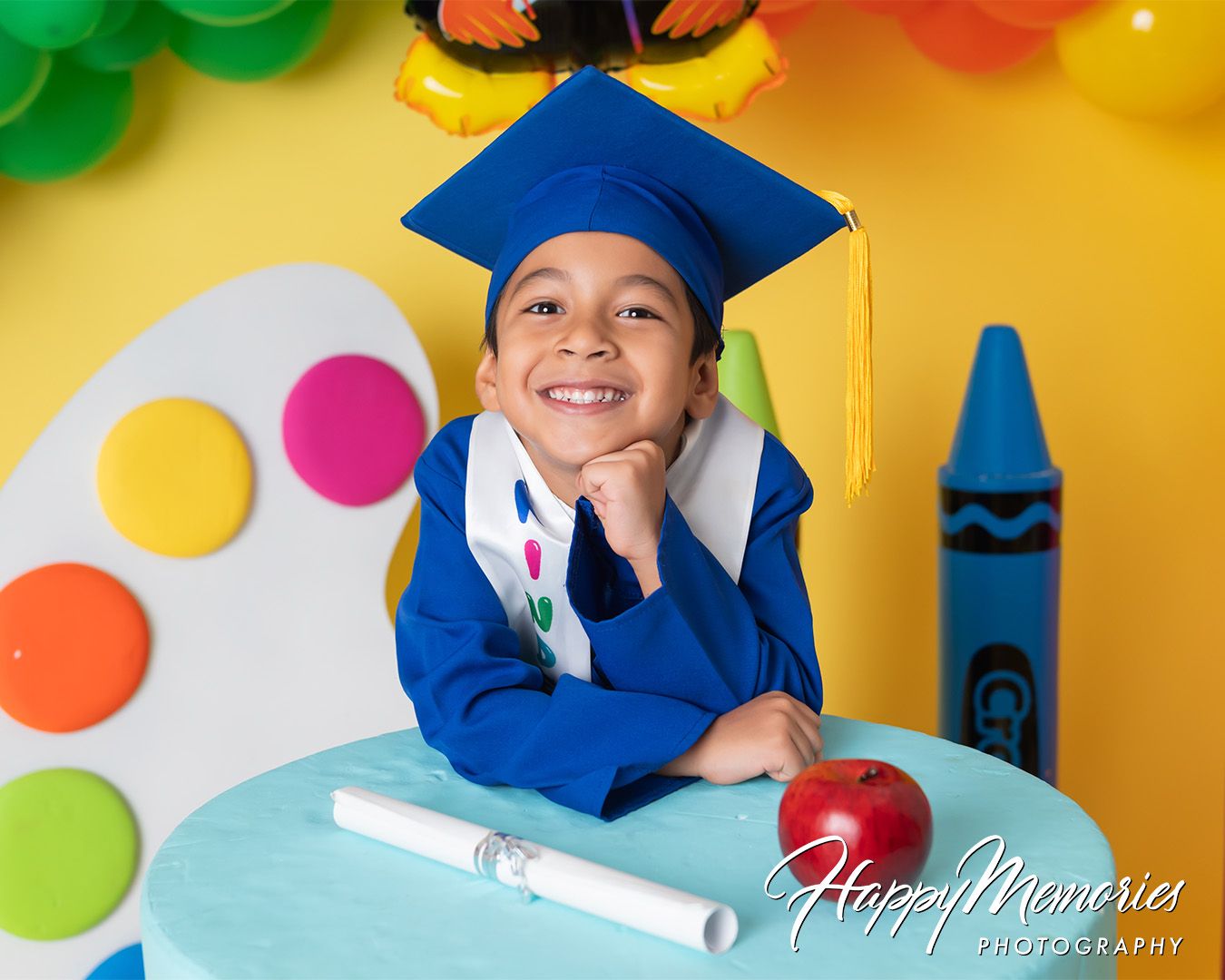 Cheerful graduation themed photo setup with rainbow balloons and art supply decorations.