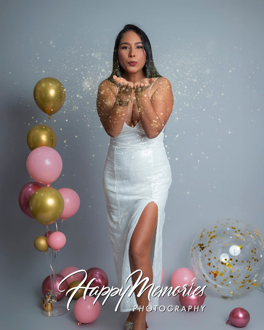 Festive photoshoot with white dress, gold and pink balloons, and glitter against grey backdrop.