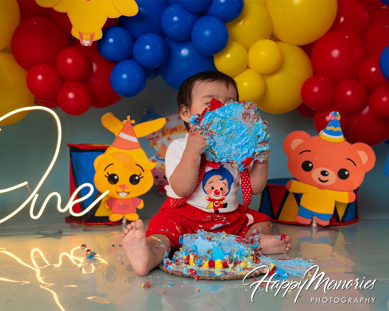 Circus themed cake smash setup with vibrant red, yellow and blue balloon decorations.