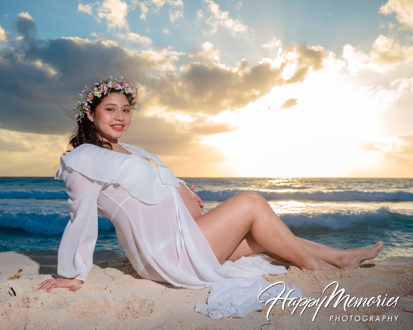 Romantic beach photoshoot at sunset with white flowing dress and ocean waves in the background.