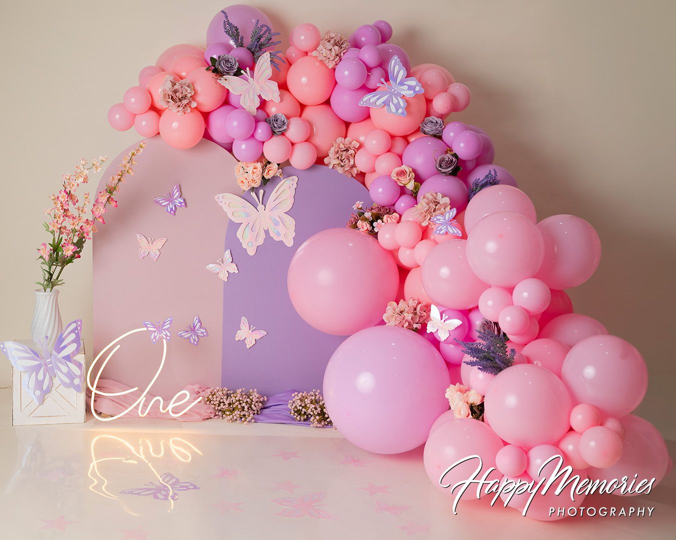 Pink balloon arch with purple butterflies and floral decorations creates a romantic backdrop for photography.