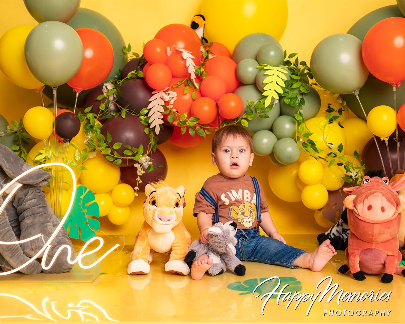 Safari themed first birthday party setup with orange, yellow and gray balloon decorations and jungle animal props.