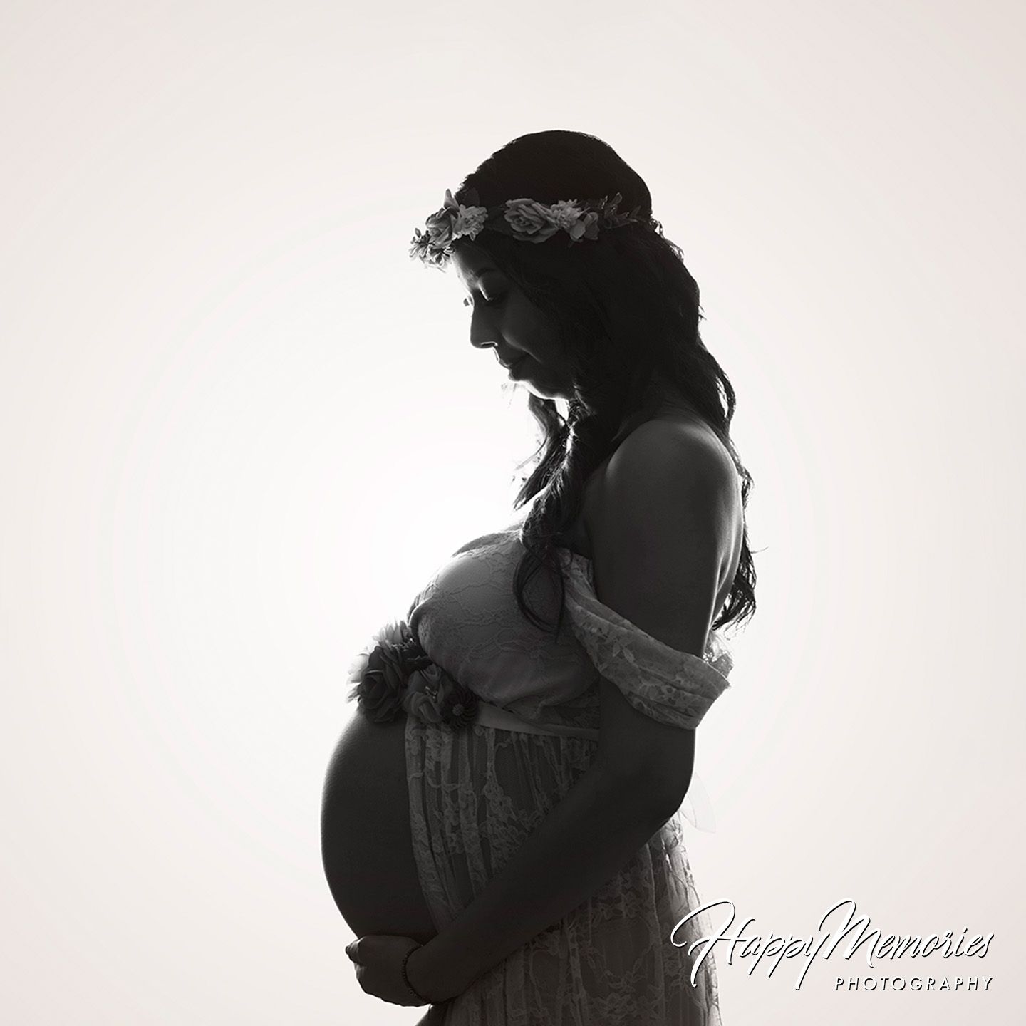 Black and white silhouette of pregnant woman in floral crown cradling baby bump in studio maternity photo.