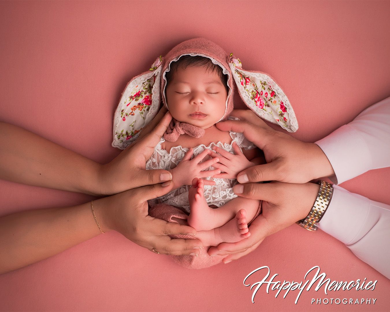 Newborn photography series showing delicate hands cradling a sleeping baby against a pink backdrop.