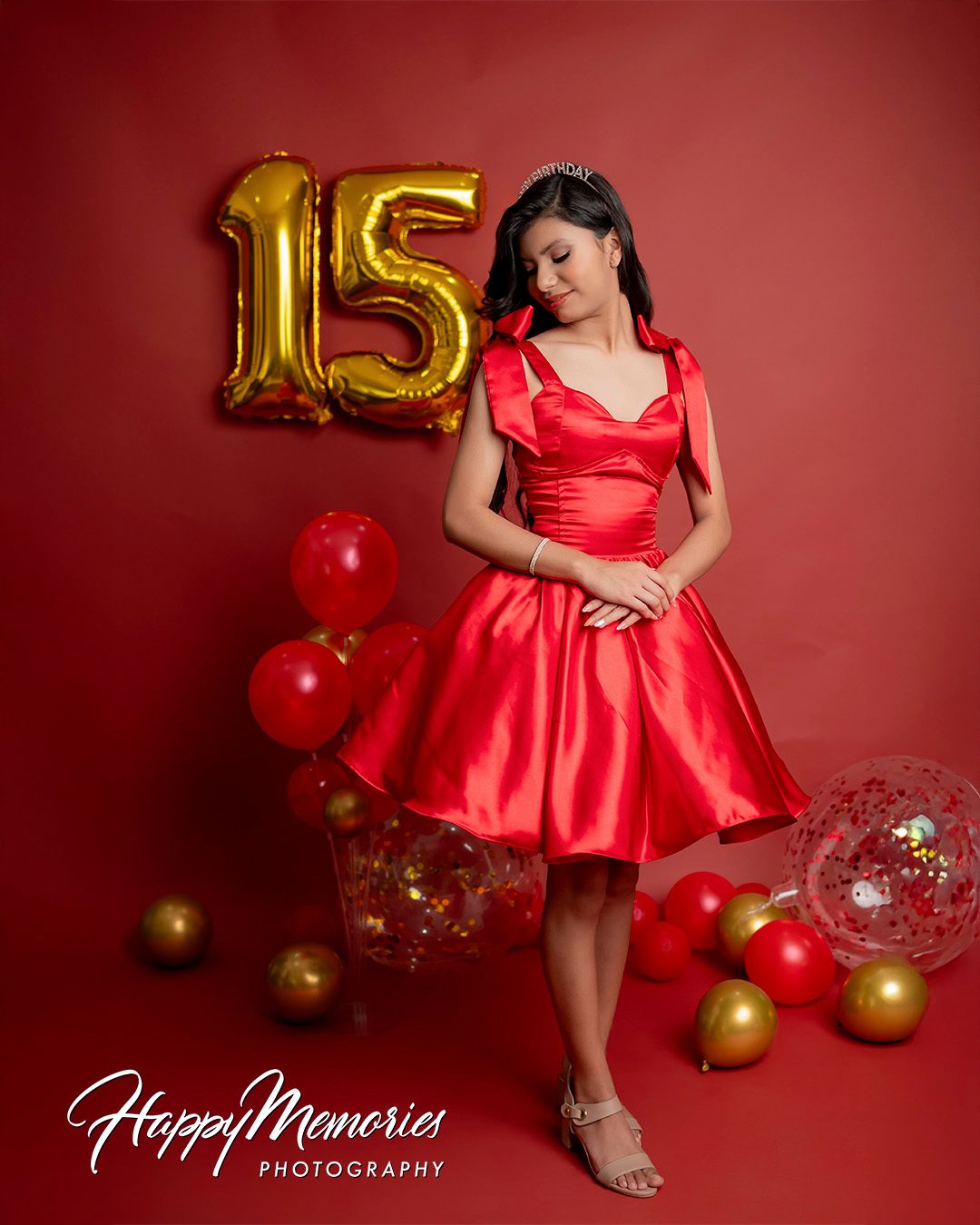 Celebratory photoshoot featuring a red party dress and gold number balloons against red background.