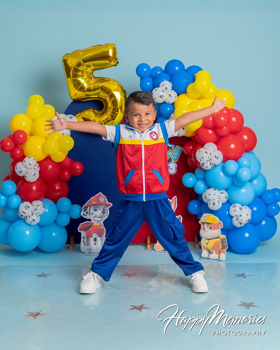 Boy in Paw Patrol outfit celebrates 5th birthday with colorful balloon arch backdrop at Happy Memories Photography.
