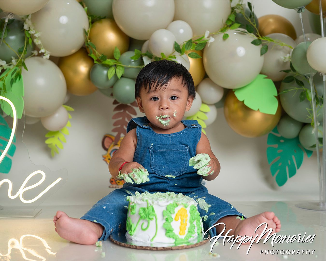 Jungle safari themed first birthday setup with white and gold balloons and tropical greenery.