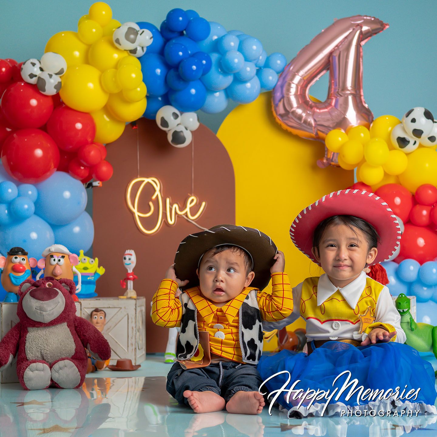 Two children in Toy Story costumes celebrate a 4th birthday with colorful balloon arch and Toy Story character decorations.