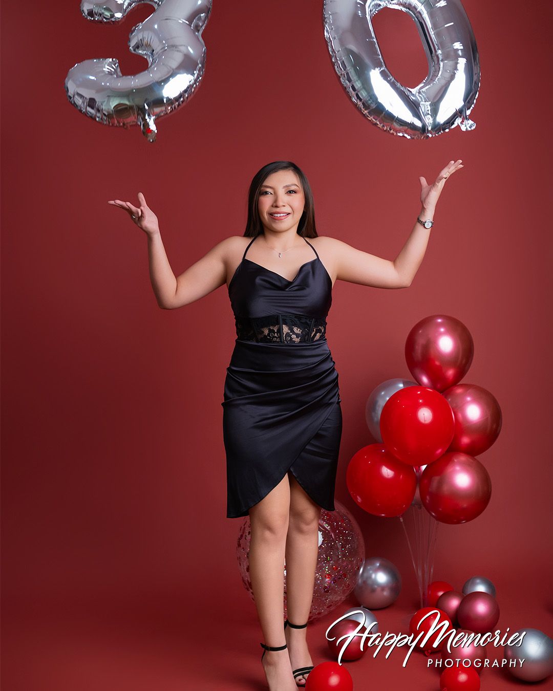 Quinceañera celebration with red balloons and a black dress against a red backdrop.