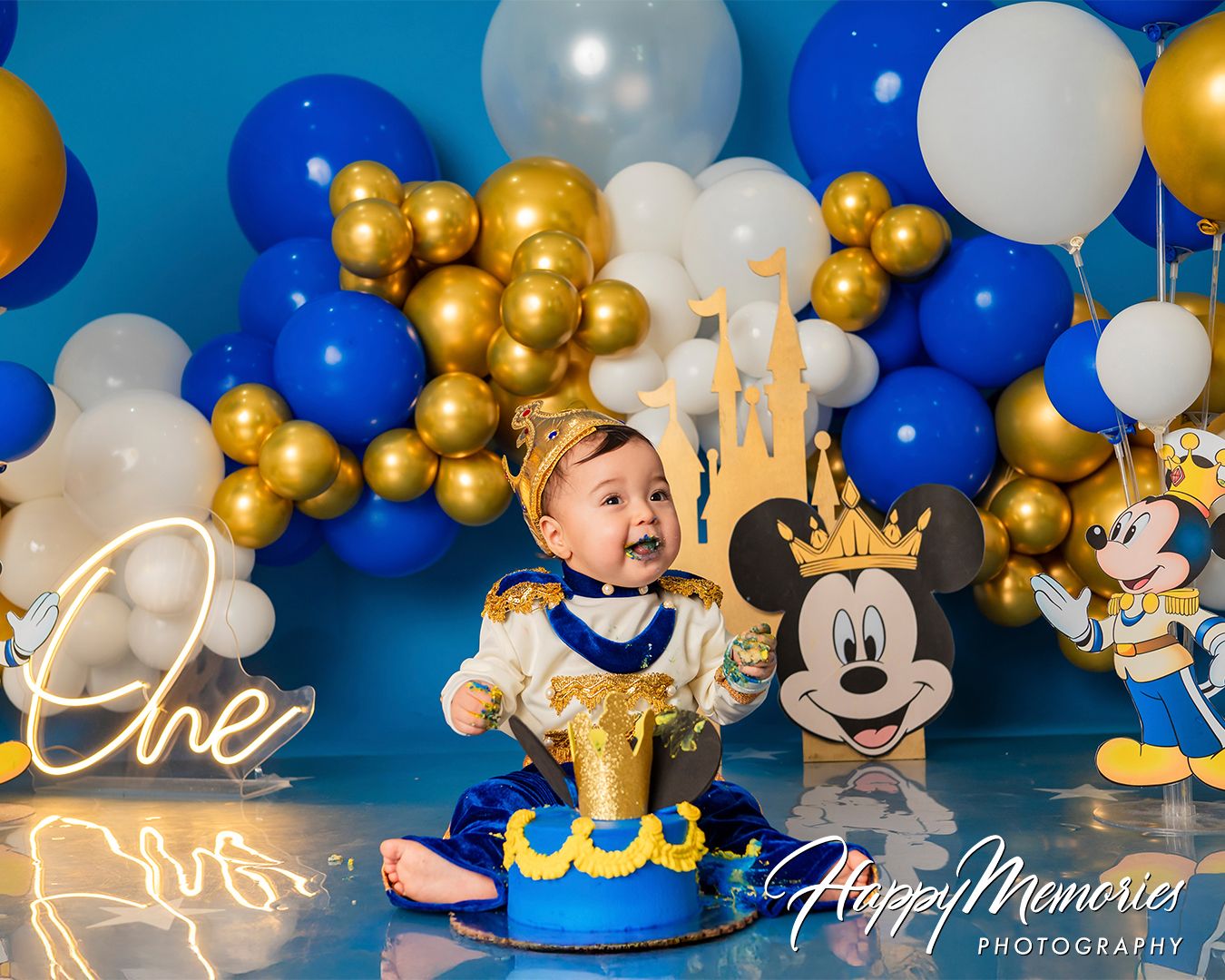 Mickey Mouse themed celebration with blue, gold, and white balloon arch and Disney character cutouts.