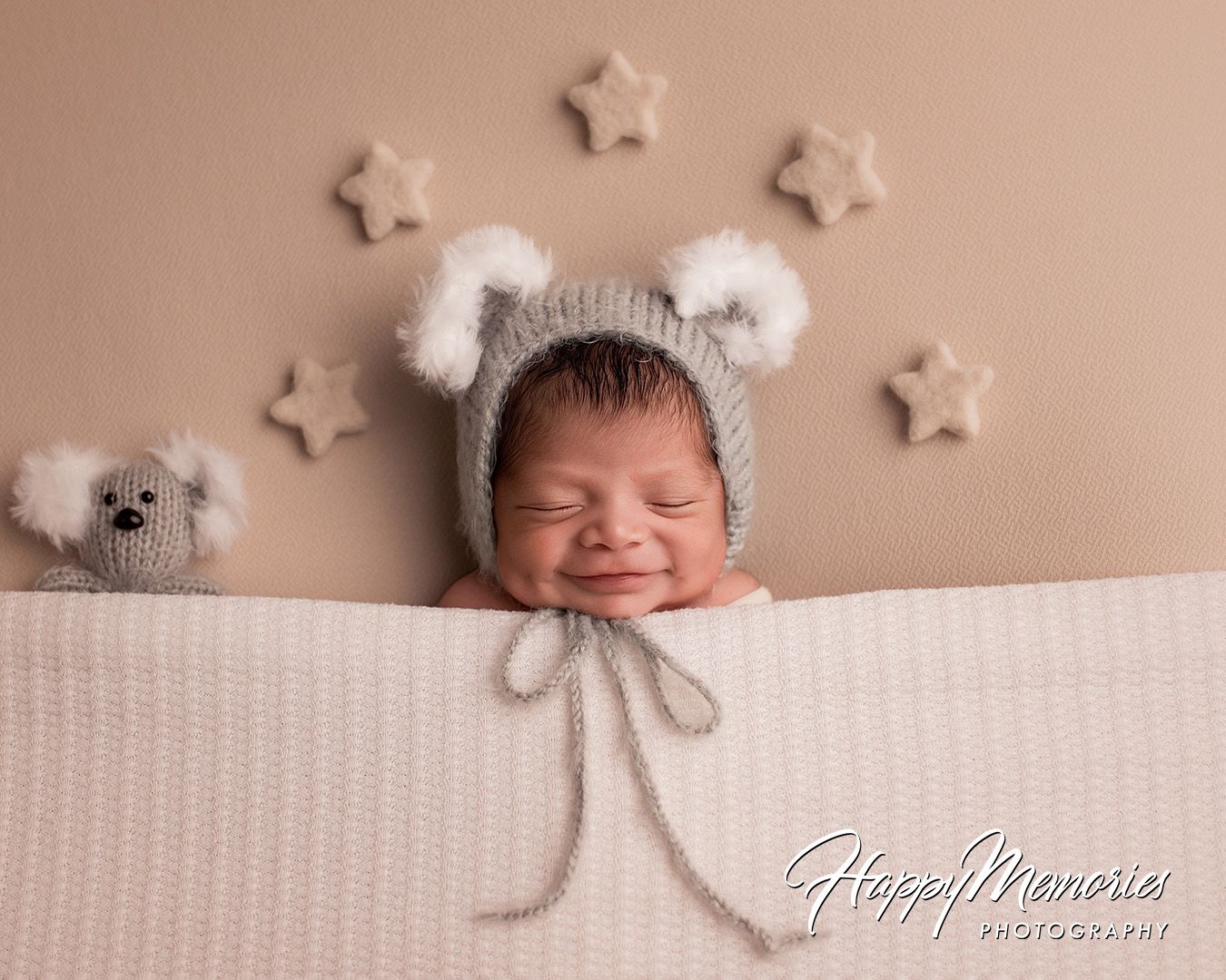 A newborn baby sleeps peacefully in a white knit hat with bear ears while surrounded by star decorations.