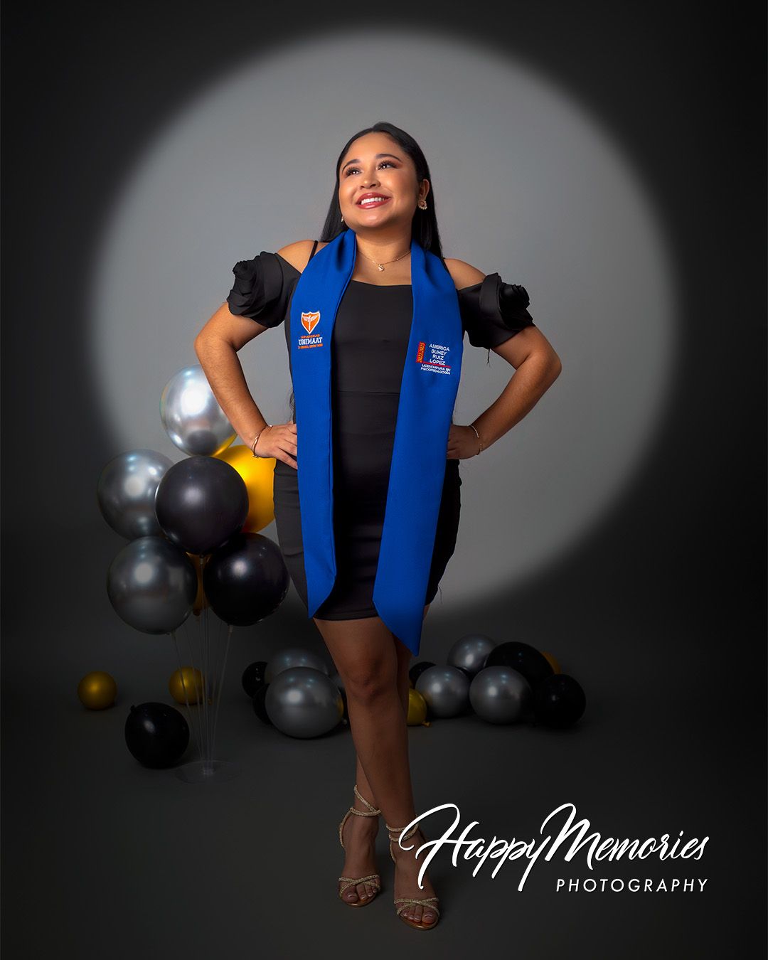 Graduate wearing blue academic stole poses dramatically against dark studio background.