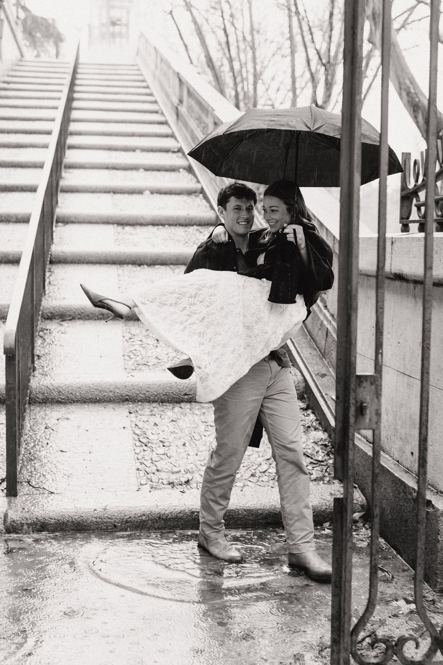 Black and white vintage photograph showing a couple sharing an umbrella on snowy steps in winter.