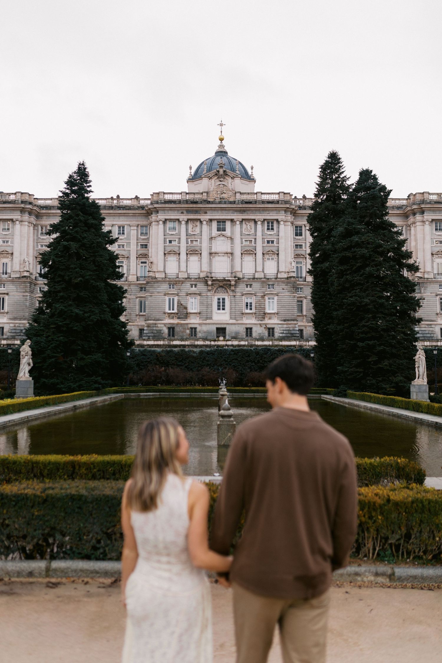 A couple admires the grand Royal Palace of Madrid and its manicured gardens from different viewing angles.