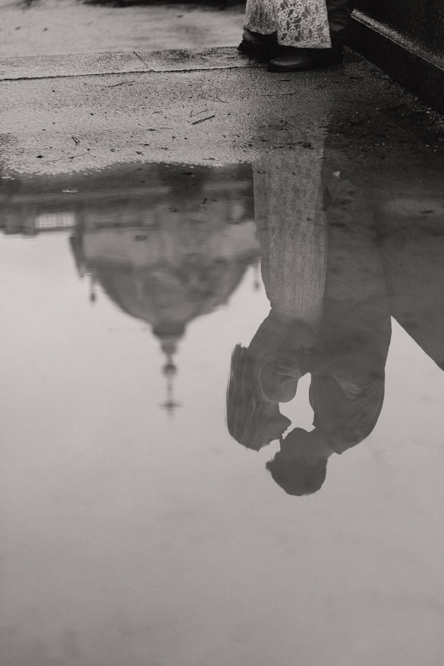 Reflections of people and buildings in a puddle of rainwater on a dark street surface.