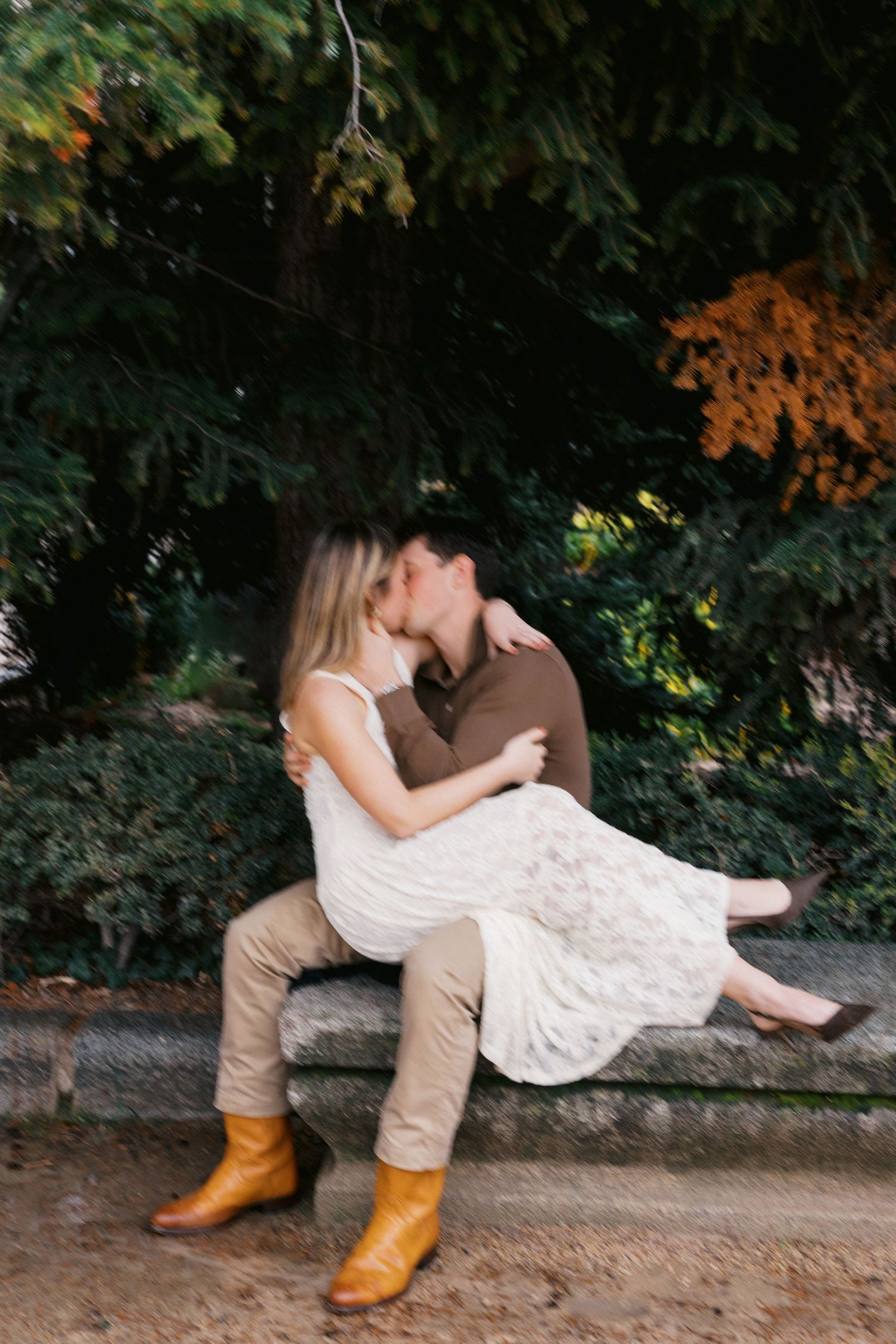 A romantic couple in western boots share a tender moment on a stone wall surrounded by autumn foliage.