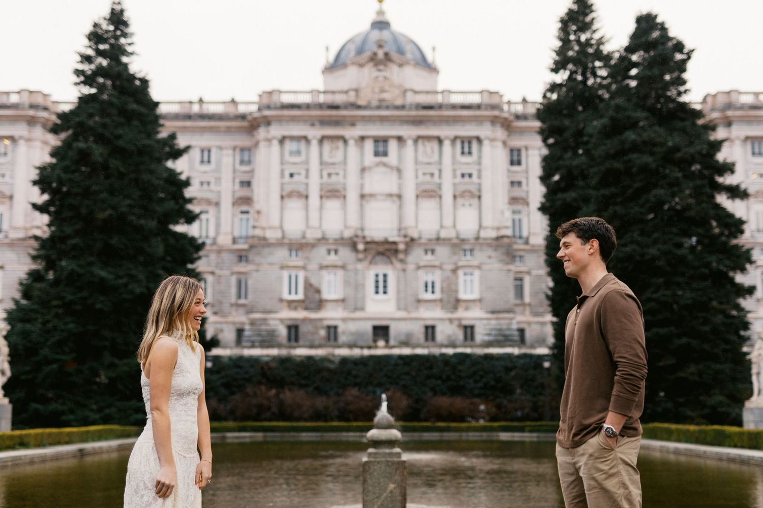 Elegant couple poses in front of the Royal Palace of Madrid during a romantic engagement photoshoot.