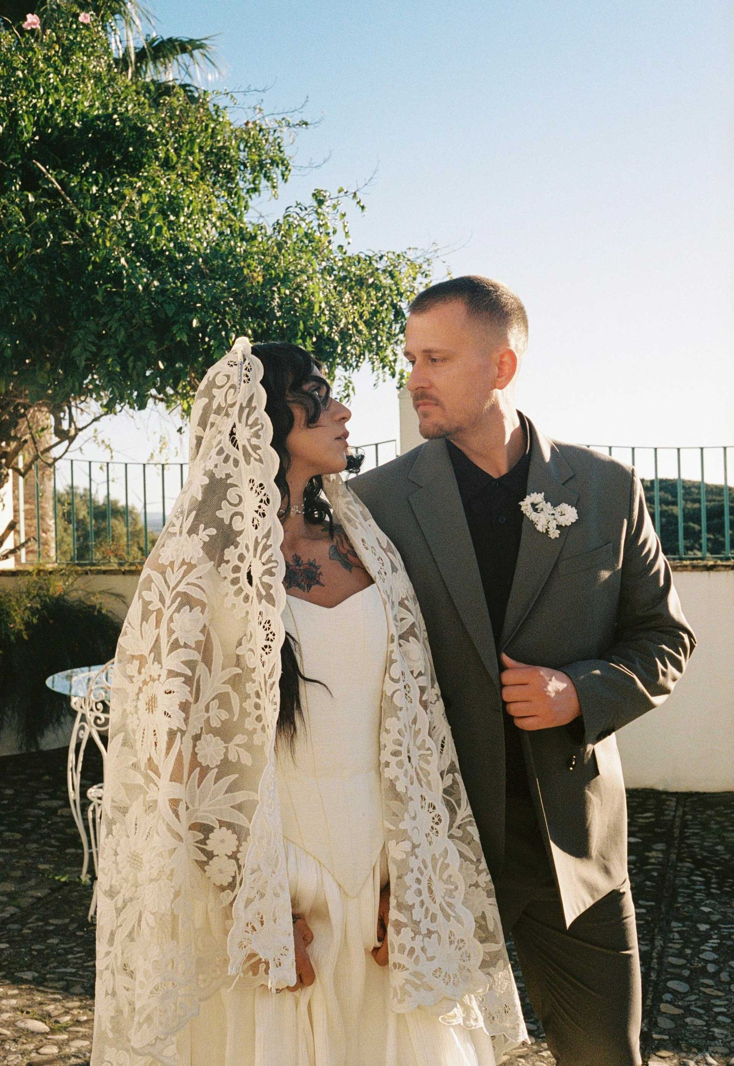 A couple shares a tender moment outdoors in wedding attire, with the bride wearing an elegant lace veil and white dress.
