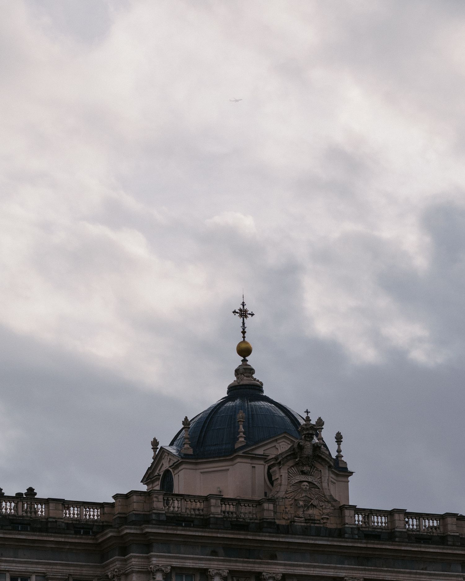 A domed church spire with a cross and ornate architectural details rises against a cloudy gray sky.
