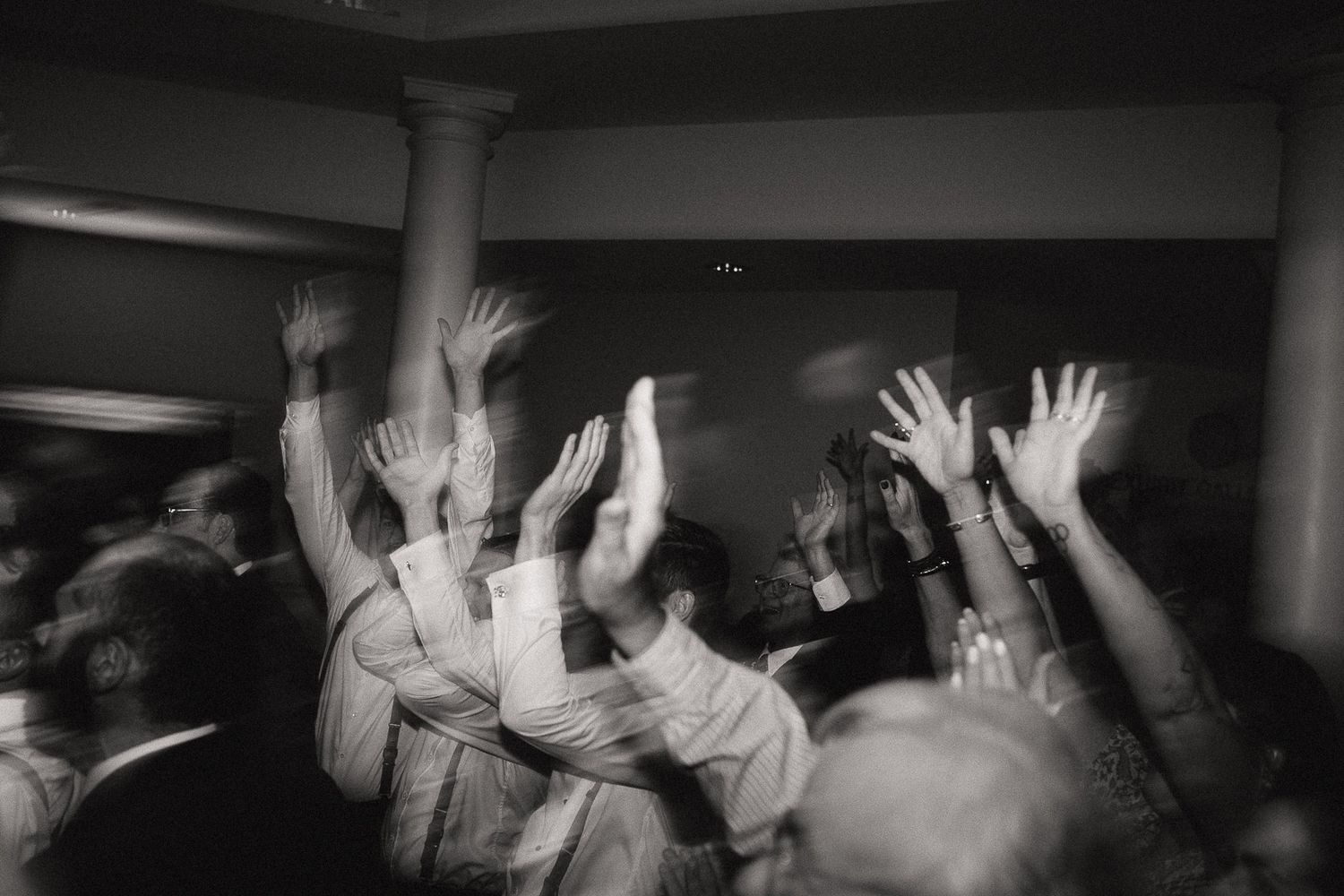 Black and white photo of people raising their hands in celebration while dancing at a wedding reception at Marquette Regional History Center