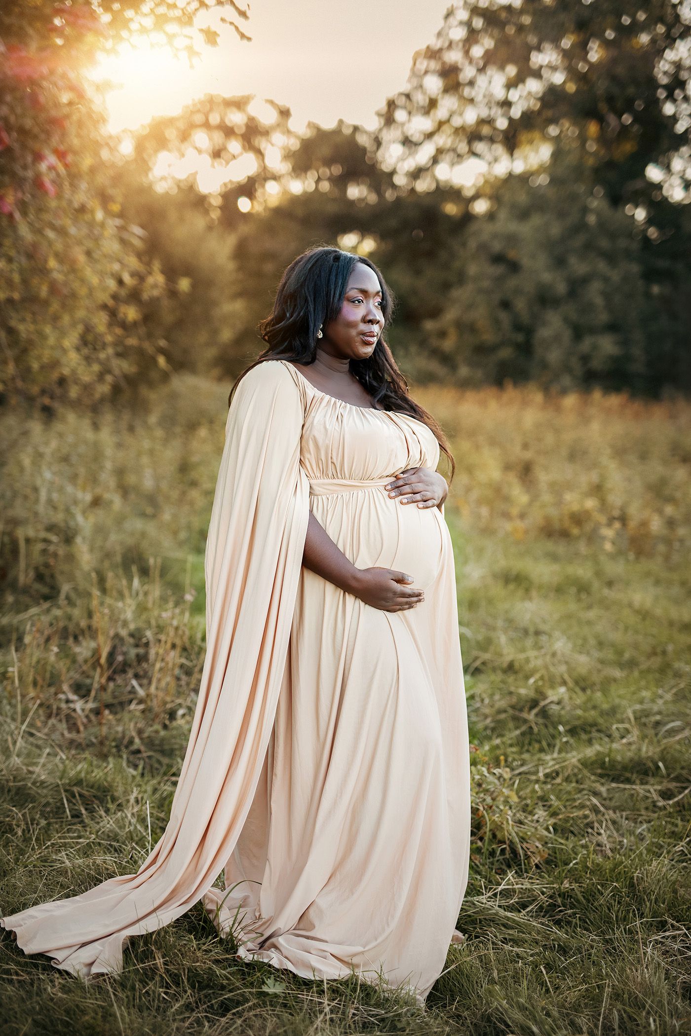 Vacker gravidkvinna i vacker klänning står i det gröna fältet och håller om sin gravida mage.