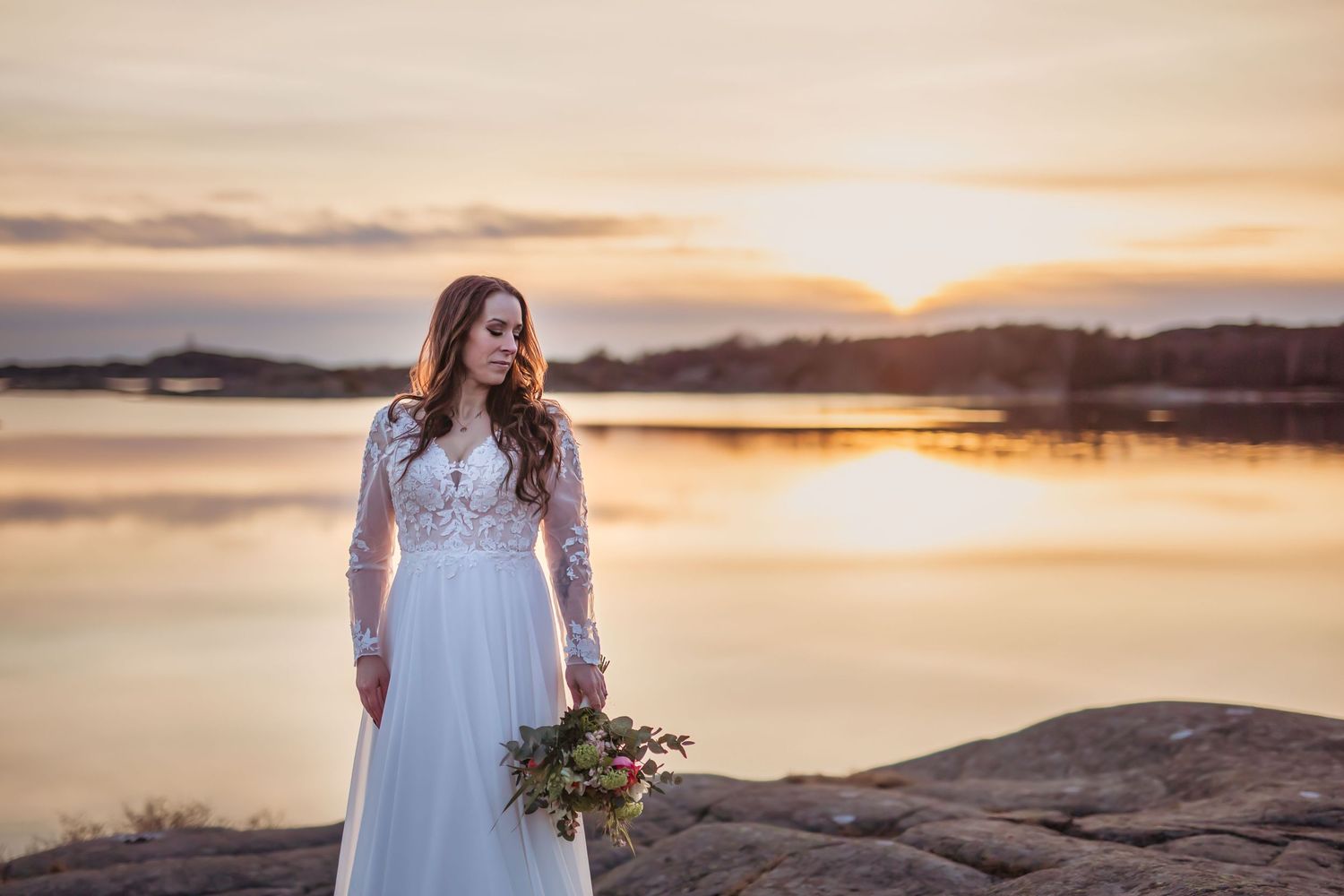 Brud i vacker bröllopsklänning vid solnedgång vid havet. Håller blombukett. Bröllopsporträtt.