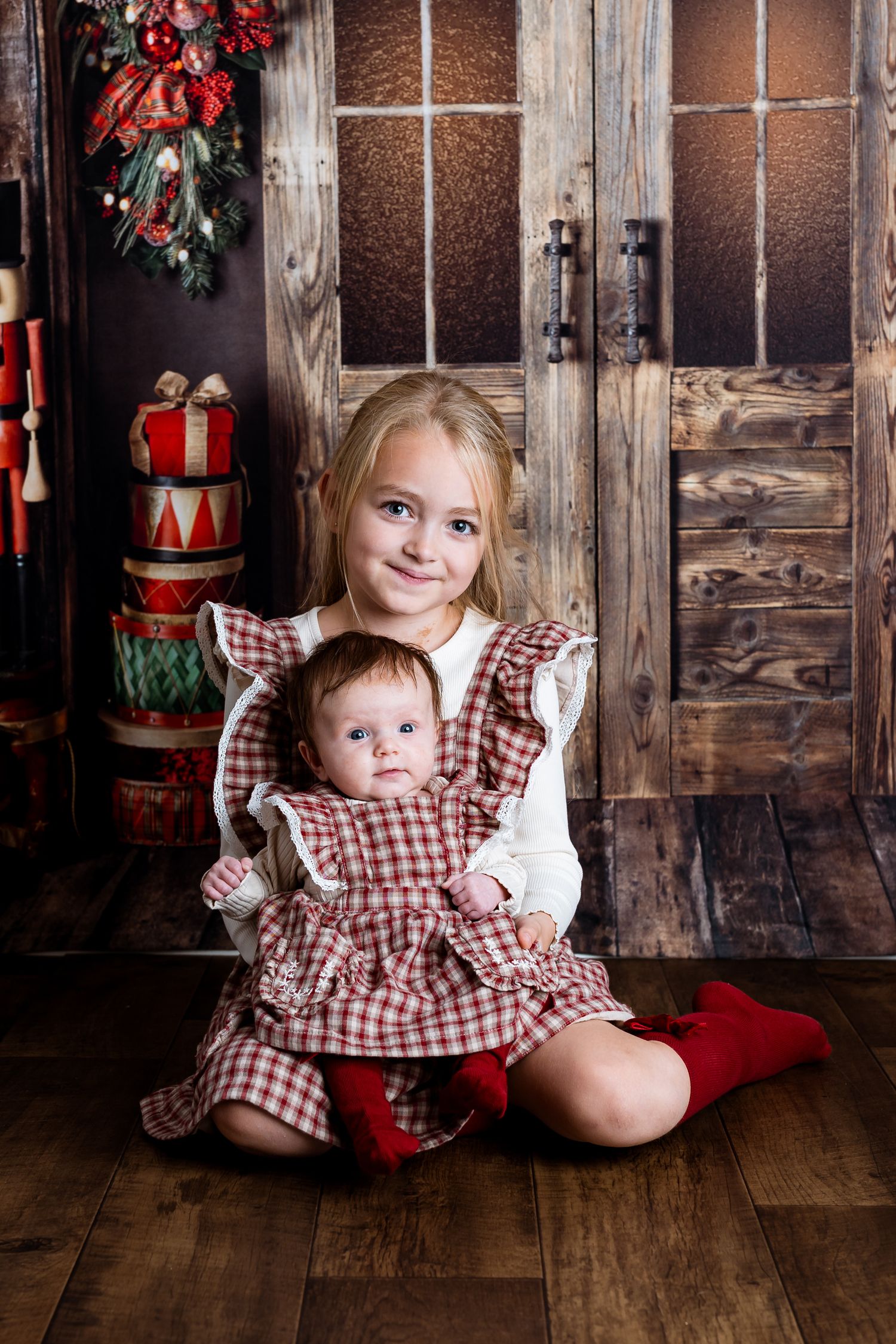 Holiday portraits with matching red gingham dresses against rustic wooden background with Christmas decor.
