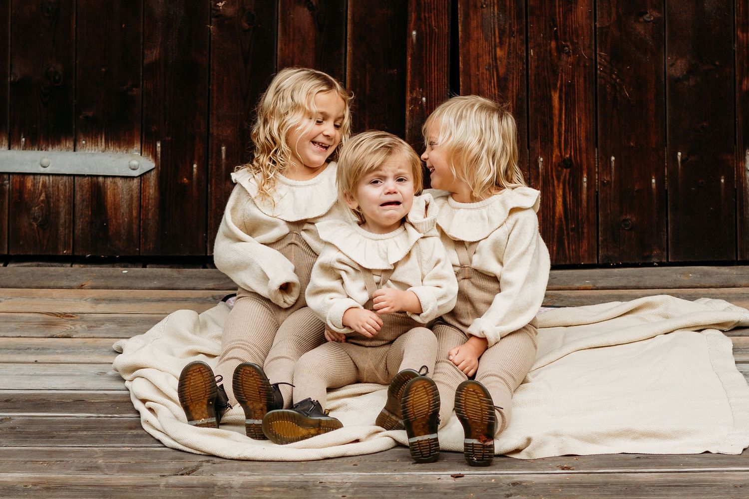 Children in cream colored outfits sitting on wooden floor.