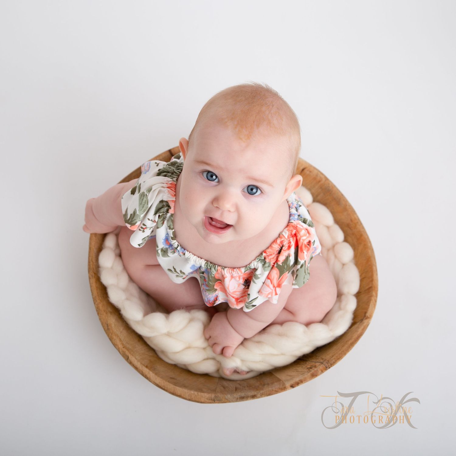 Baby lying in wooden bowl prop with floral decorations during photo session.