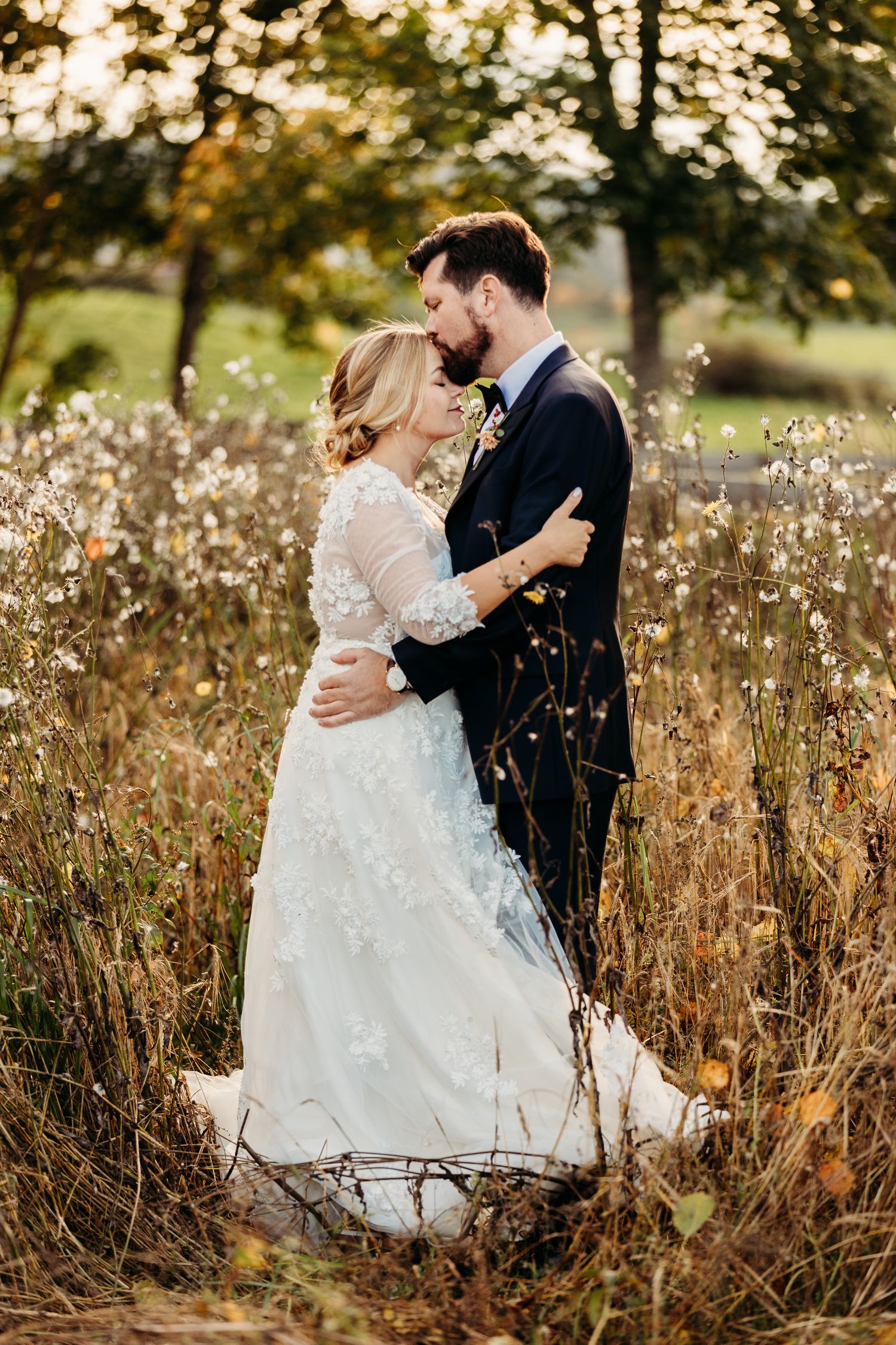 Couple embraces in tall autumn grass during golden hour wedding photoshoot.