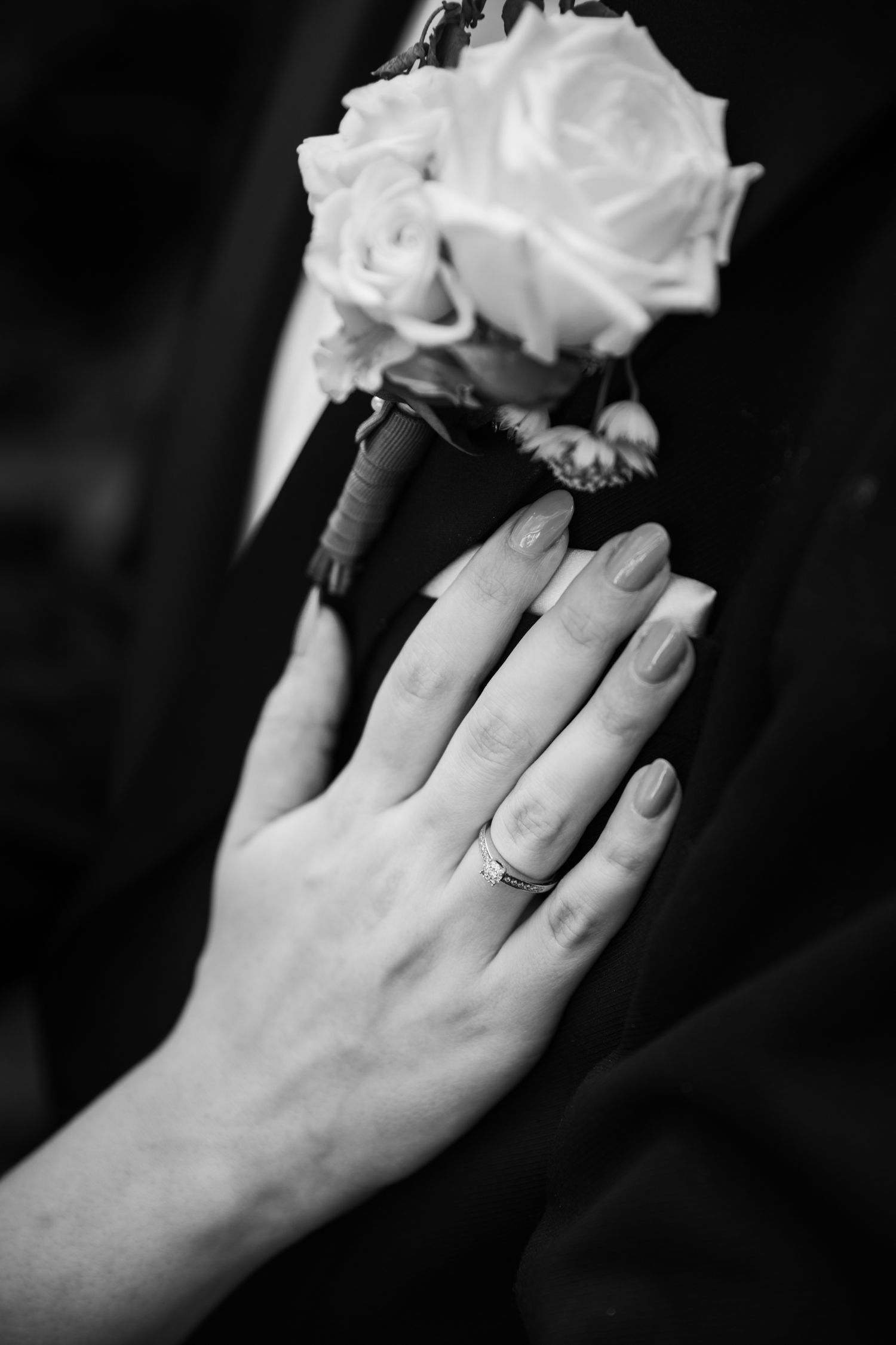 Black and white close-up of hand with wedding ring holding white rose.