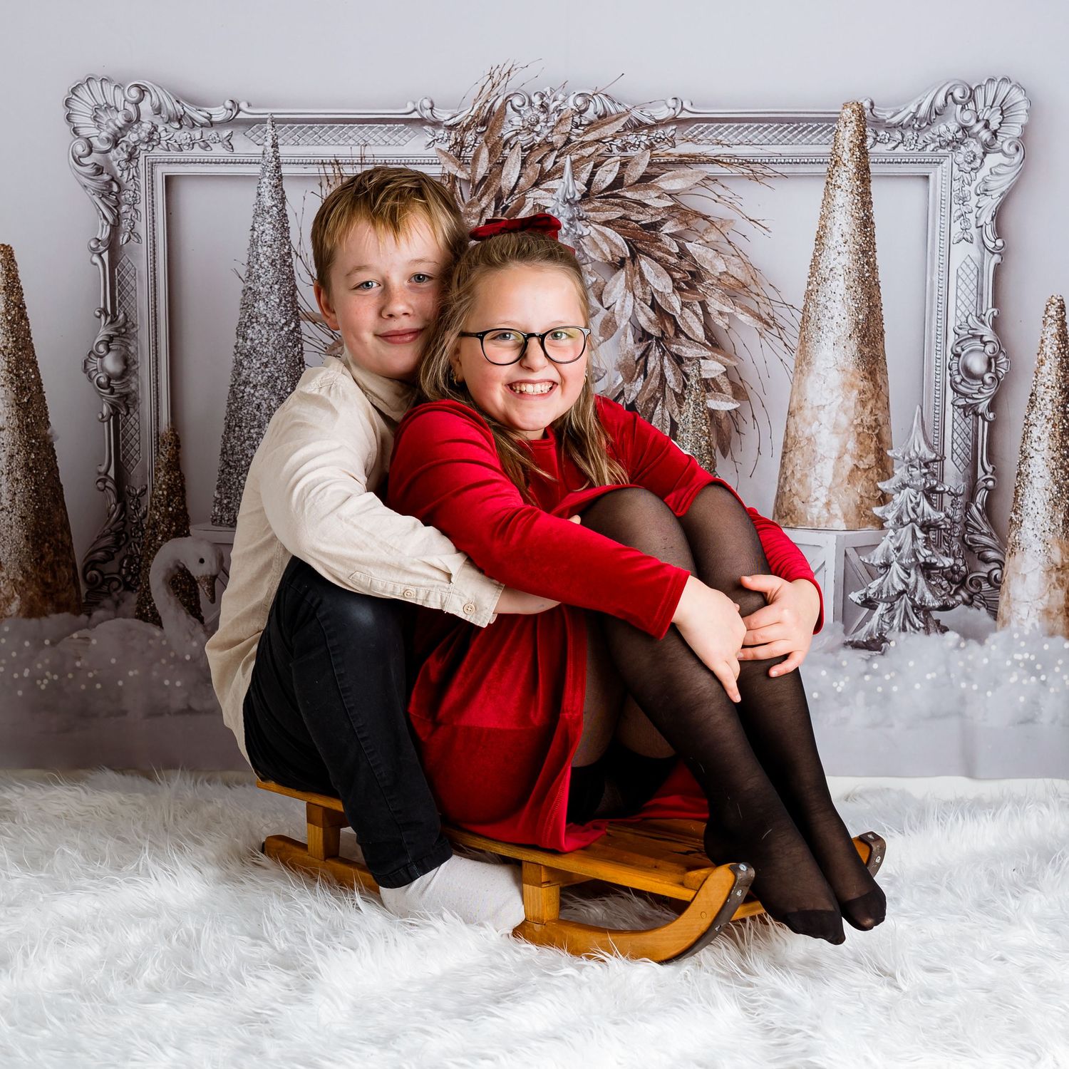 Cozy winter portrait session with children on wooden sleigh against snowy backdrop.