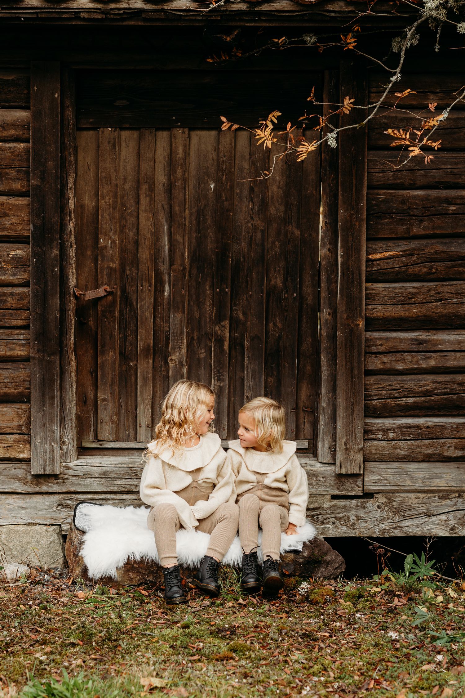 Back view of people in cream outfits sitting against rustic log cabin wall.
