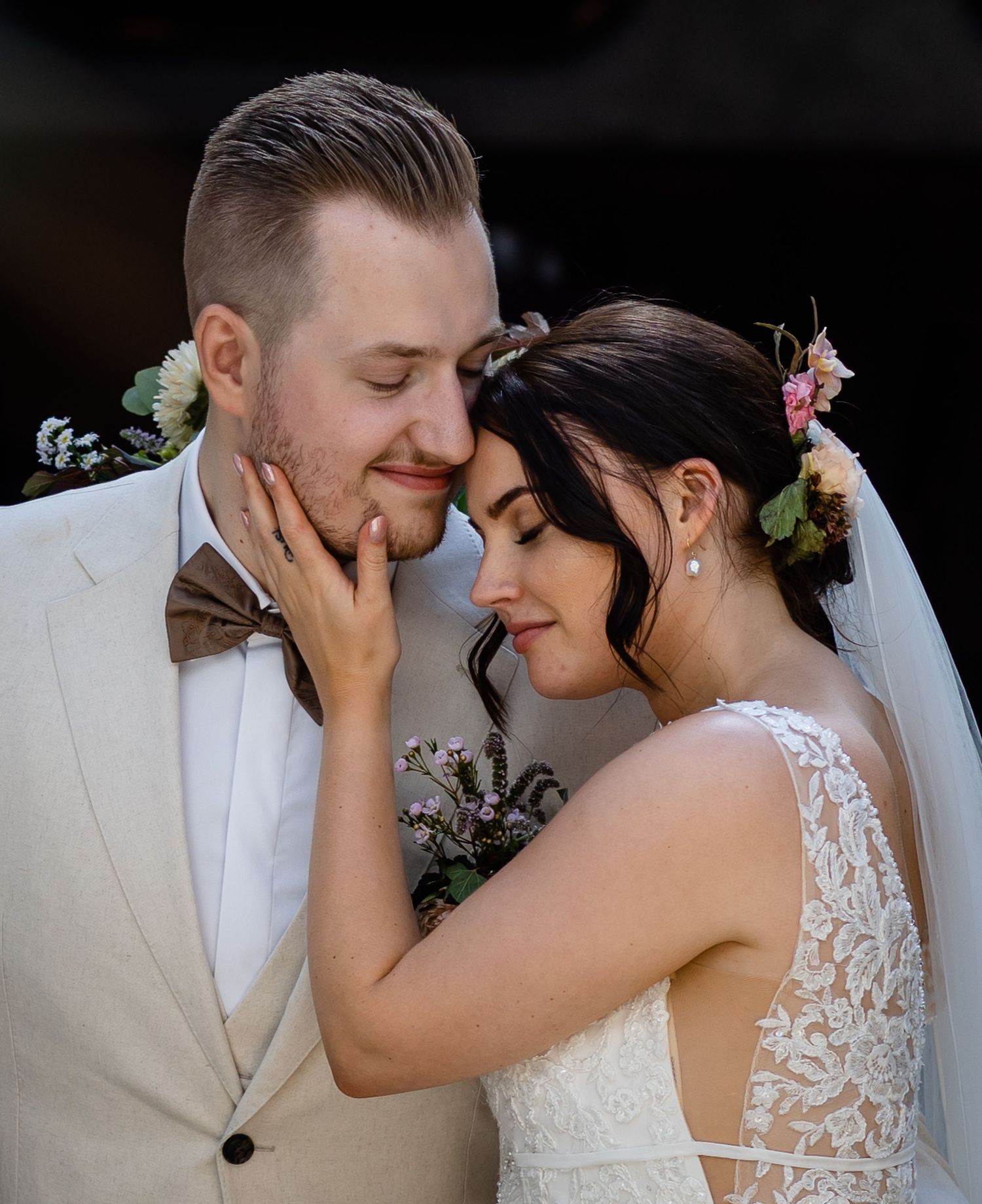 An intimate moment between newlyweds in white attire with floral accents.