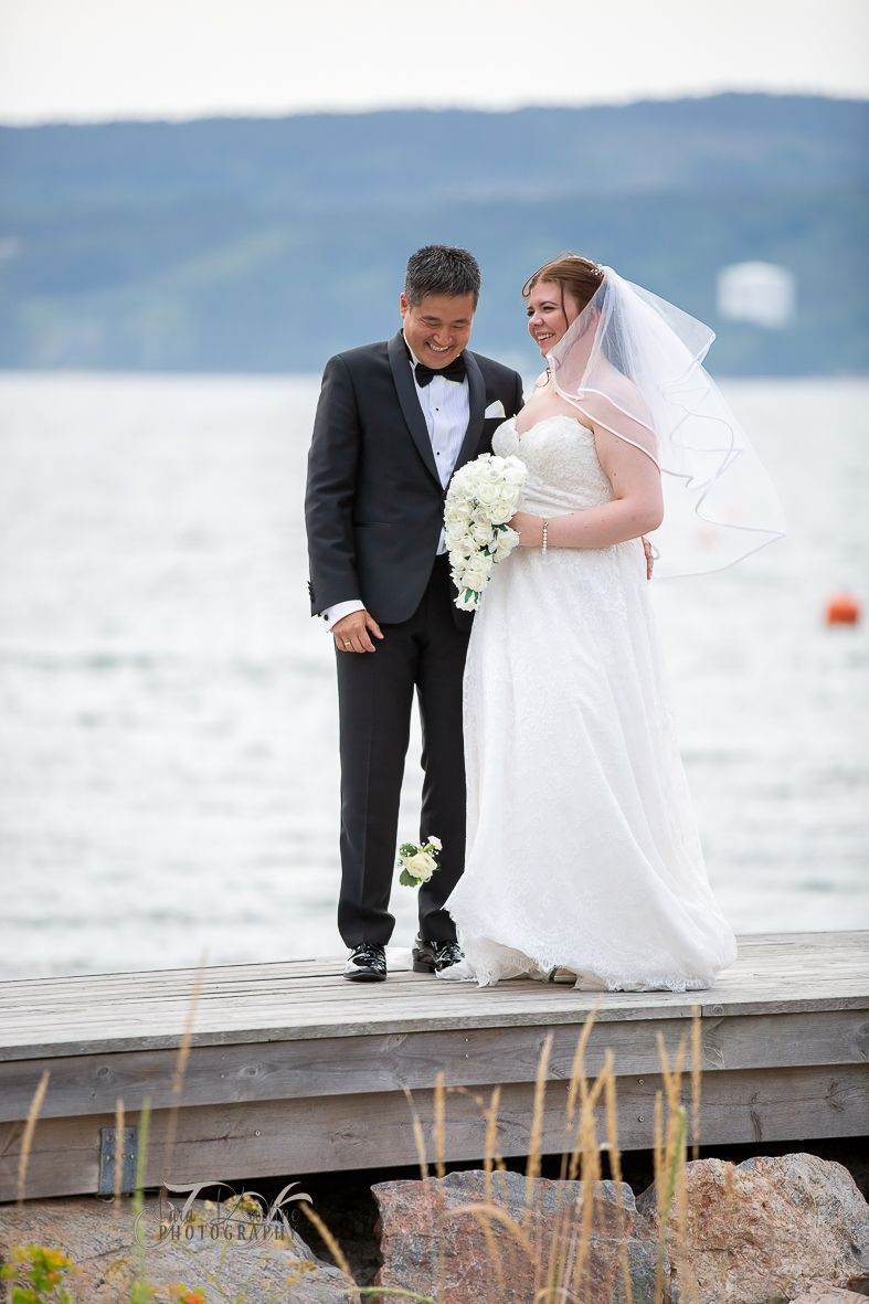 Wedding couple standing on a wooden dock by the water.