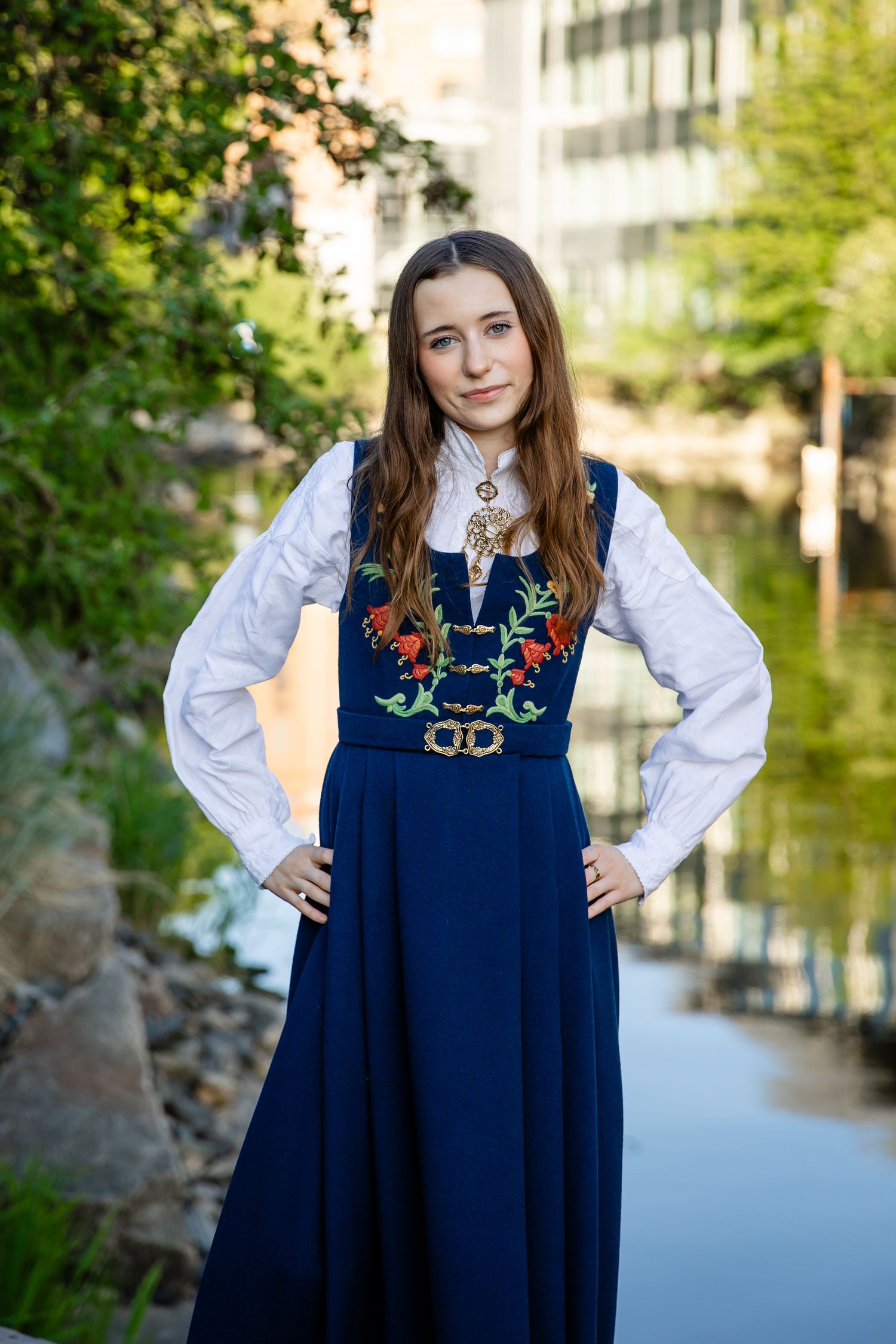 Navy blue Norwegian folk dress with colorful embroidery shown against waterfront background.
