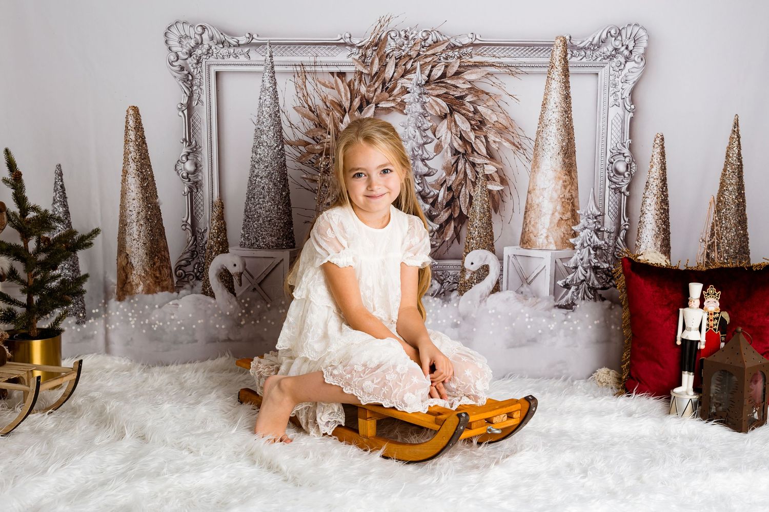 Child sitting on vintage wooden sled surrounded by gold trees and holiday decorations.