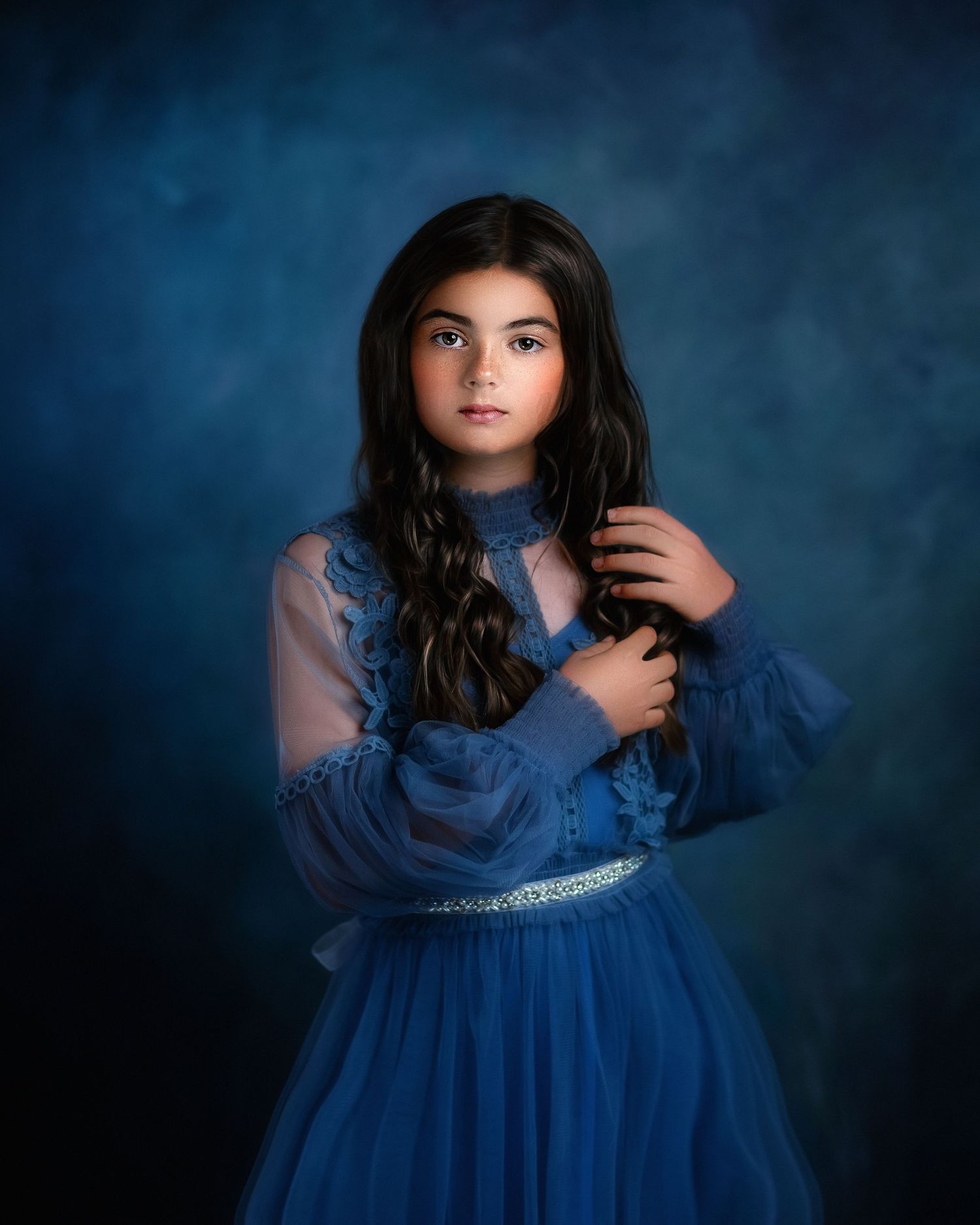 Dramatic portrait in blue dress against dark moody background.