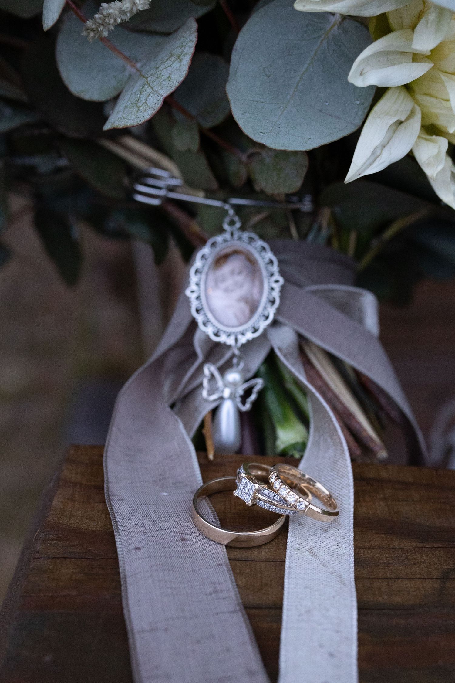 Wedding rings and jewelry details arranged on rustic wooden surface with white floral accents.