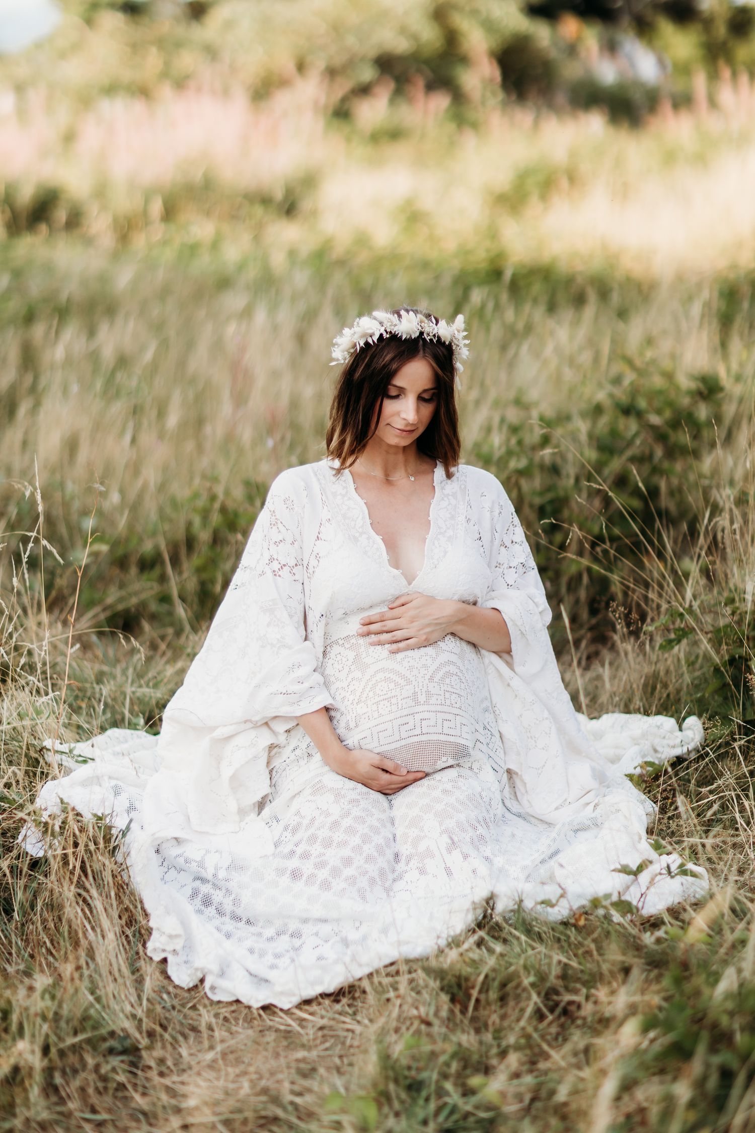 Maternity portrait series featuring a white lace dress in a natural outdoor setting.
